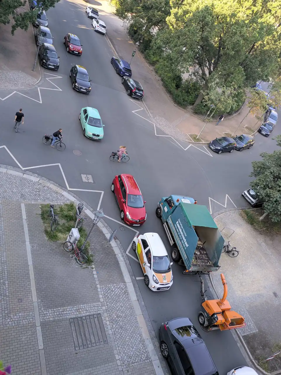 Luftaufnahme der komplexen Verkehrssituation am Stresemannplatz: Eine belebte Kreuzung mit Autos, einem Lastwagen mit Holzhäcksler, Radfahrern und einem Kind auf dem Fahrrad. Das Bild visualisiert den Konflikt zwischen Autoverkehr, Fahrradfahrern und Fußgängern und die Notwendigkeit einer Verkehrswende und besseren Stadtplanung.